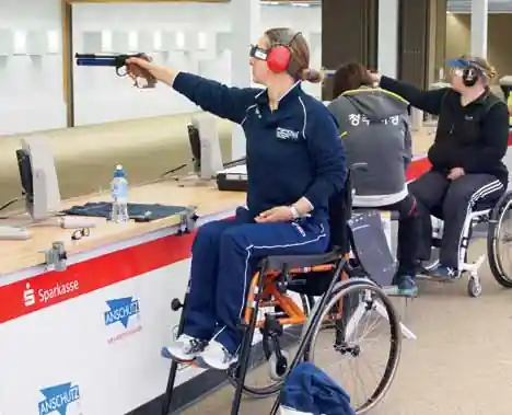 Tiratrice paralimpica in carrozzina, ripresa di lato, mentre prende la mira con una pistola ad aria compressa durante una gara.